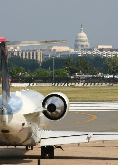 Airplane landing on a runway with Washington, DC skyline, including White House, in background